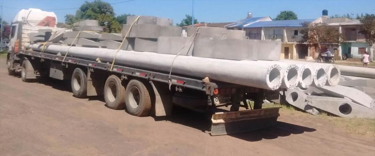 Camión semirremolque cargado con columnas de hormigón armado centrifugado y postes pretensados para obras de infraestructura eléctrica bajo normas EPE Santa Fe, EPEC Córdoba, DPEC Corrientes, EDENOR y EDESUR. Despacho directo desde planta de fabricación a loteos y barrios cerrados en Argentina, logística y transporte pesado Grupo Abinor.